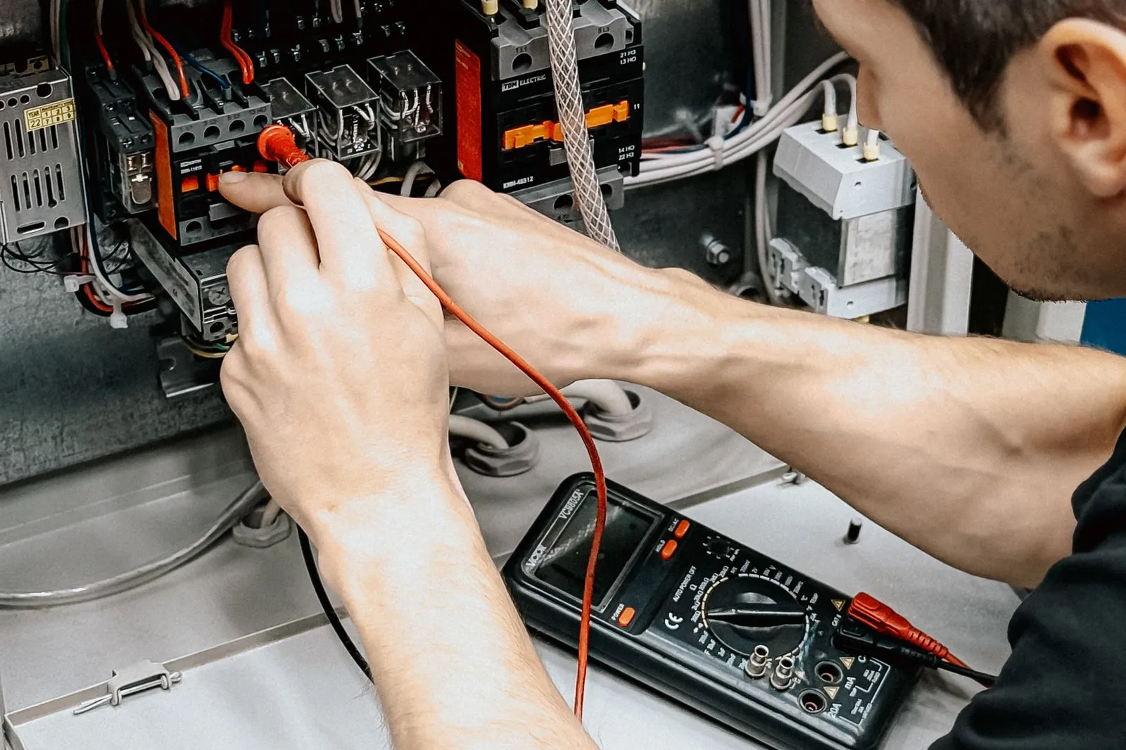 An electrician tests connections in an open electrical panel with a multimeter