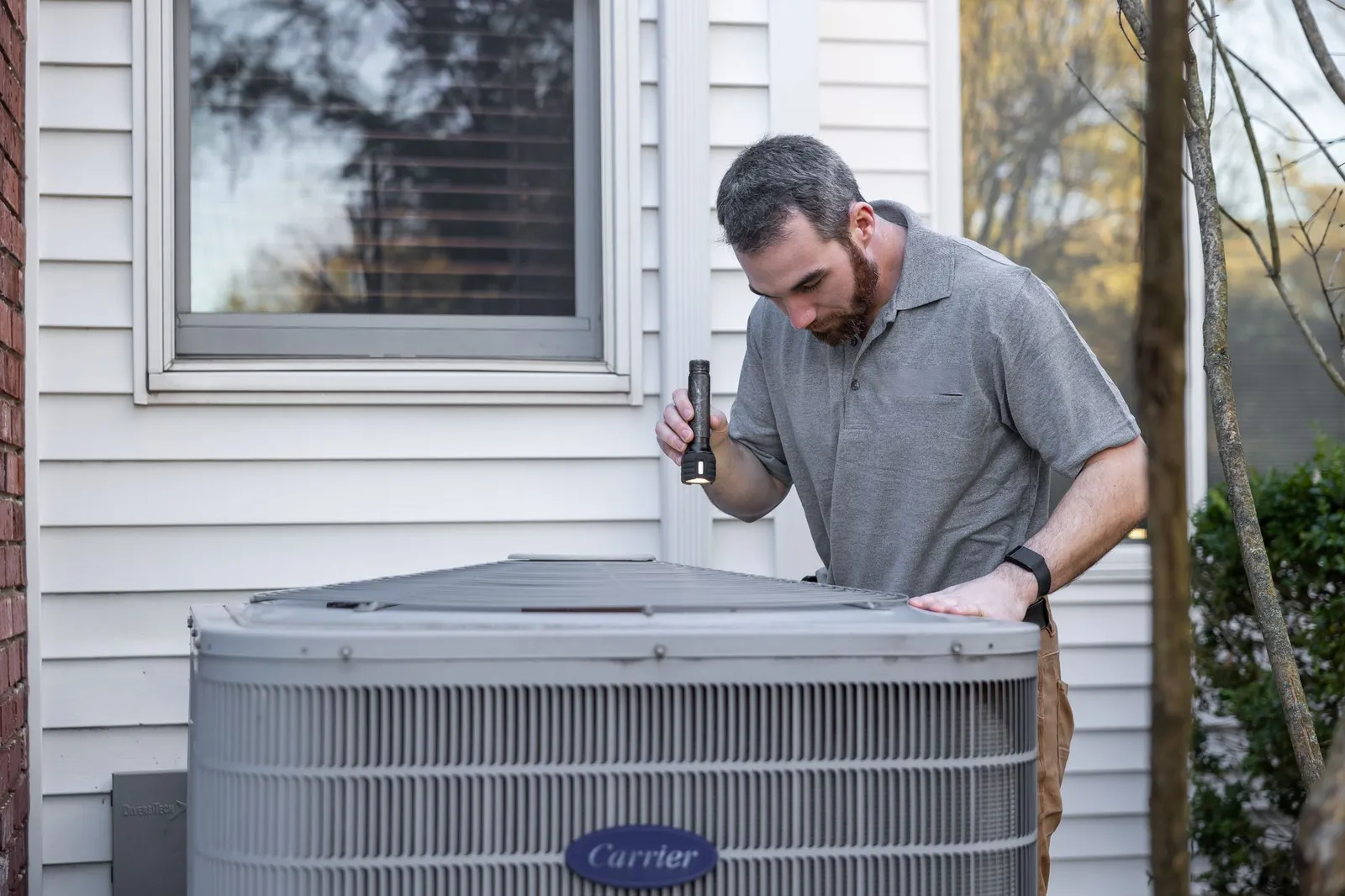 Un técnico de HVAC revisa con una linterna una unidad exterior de aire acondicionado