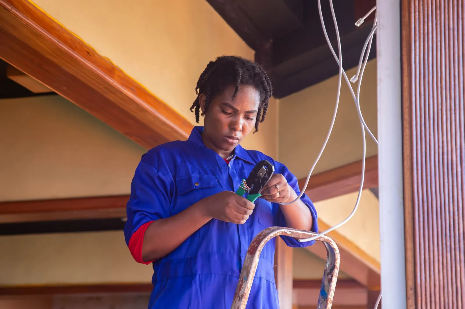 A woman electrician on a ladder holds cables during an installation